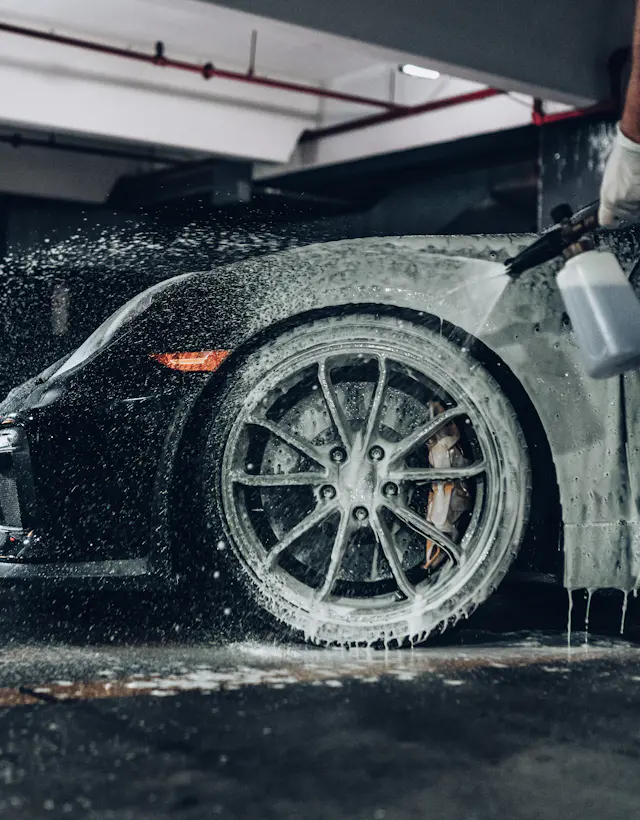 Foam being sprayed onto a black sports car in a wash bay