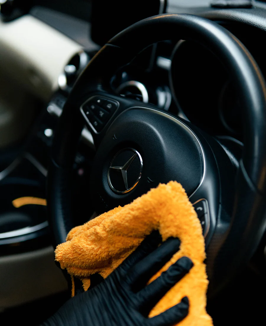 A gloved hand wiping a steering wheel with a microfiber towel